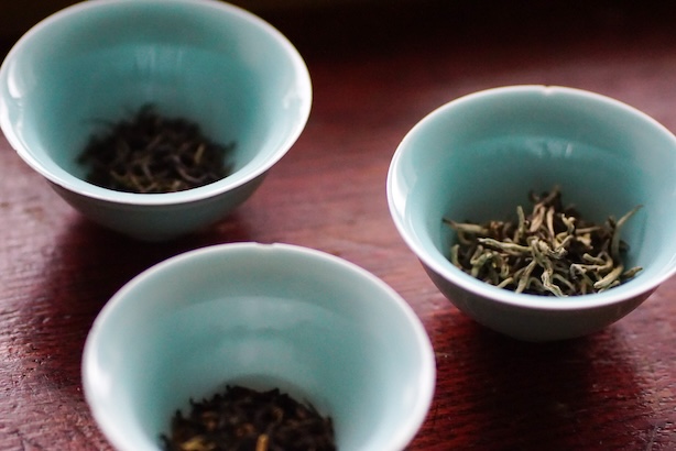 Kolme pientä, turkoosia teekuppia, joissa on irtoteelehtiä