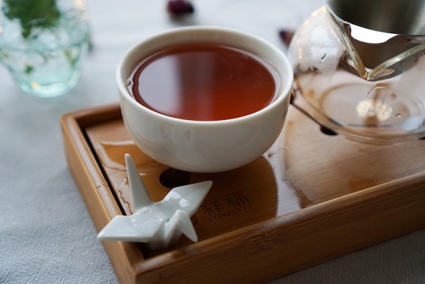 Kuva punaisesta teestä valkoisessa teekupissa, ympärillä teen haudutustarvikkeita