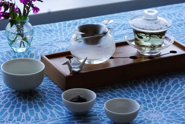 Valokuva teemaisteluastiastosta ja läpinäkyvässä gaiwanissa hautuvasta teestä