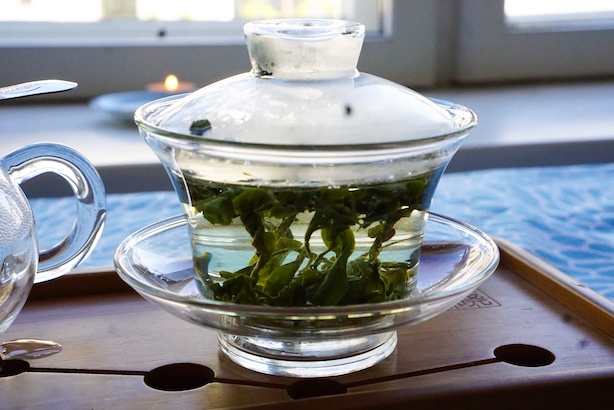 Valokuva läpinäkyvästä gaiwanista, jossa vihräet teenlehdet aukeavat