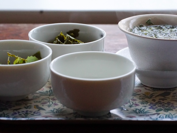 Tarjotin joaa kolme teekuppia ja yrttitee hautumassa gaiwanissa
